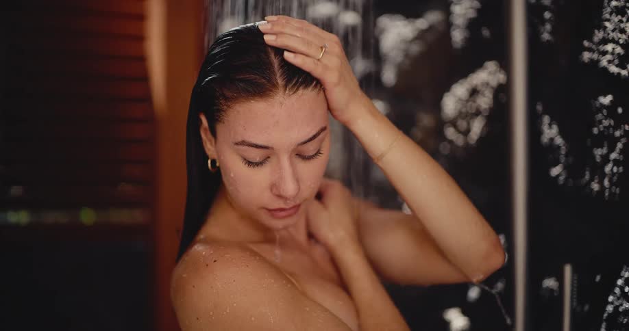 A contemplative young woman finds a moment of peace while taking a slow-motion shower, with warm water cascading over her