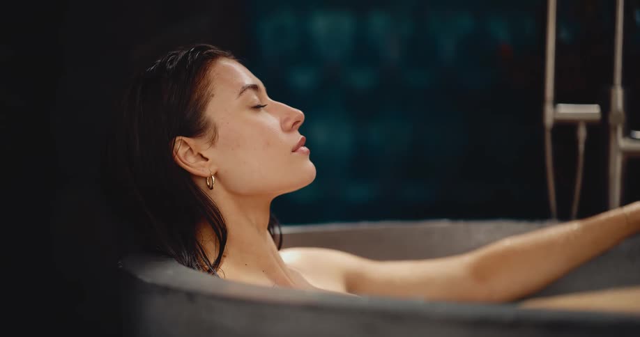 A serene woman finds a moment of peaceful contemplation while relaxing in a modern, dark bathtub