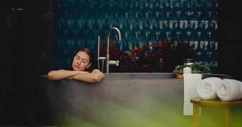 A thoughtful young woman relaxes in a modern stone bathtub in a tranquil spa setting