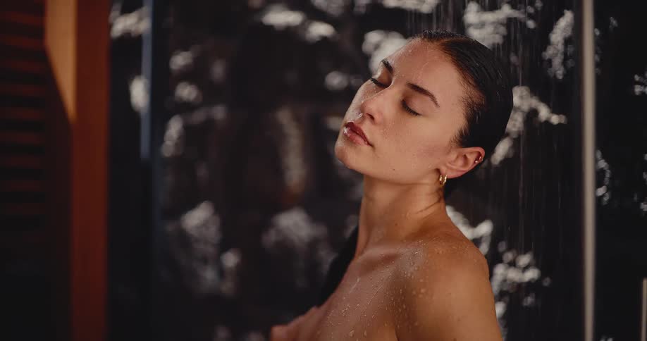 A beautiful woman relaxes in a tranquil shower, letting the warm water wash over her in slow motion