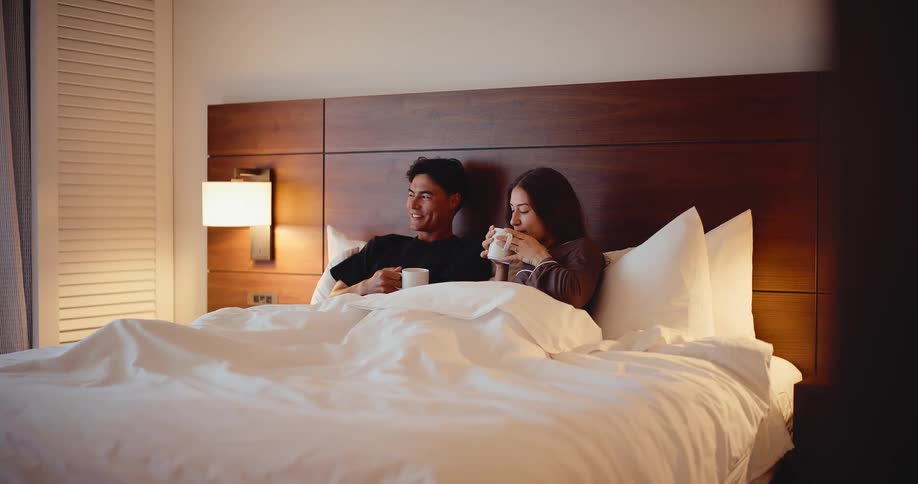 Happy young couple relaxing in bed with their morning coffee on vacation