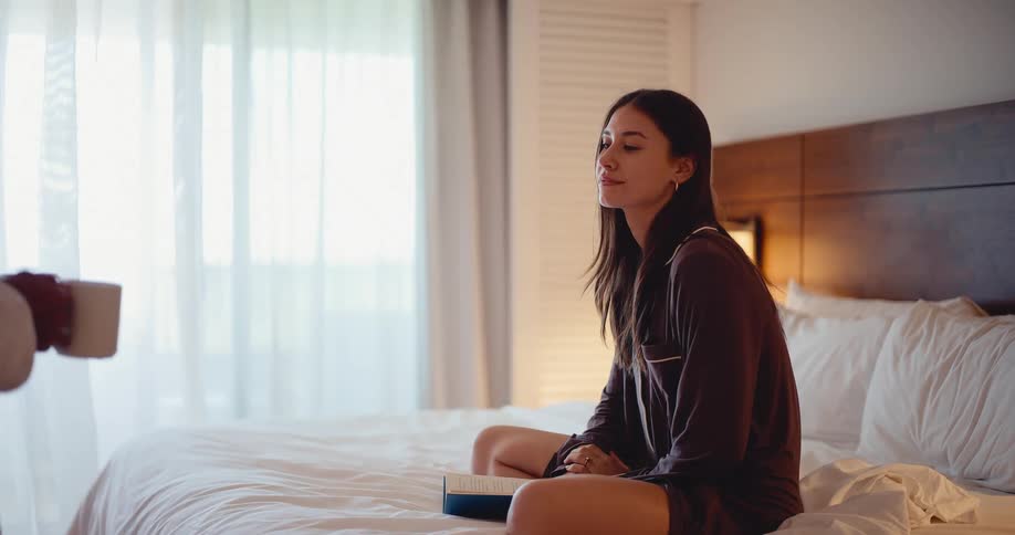 A thoughtful partner brings a cup of coffee to a woman reading a book in bed in the morning
