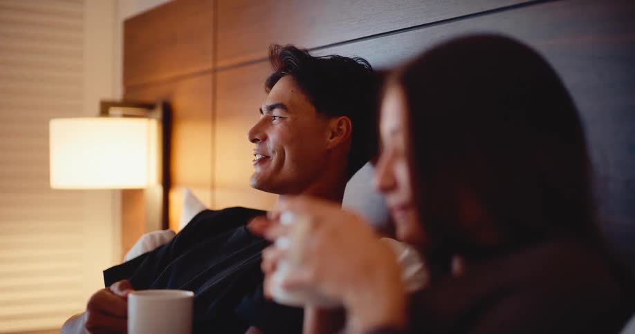 A happy young couple enjoys an intimate moment talking and smiling over coffee together in bed