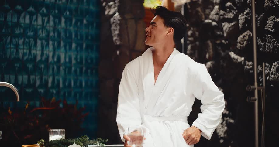 A handsome young man in a white bathrobe relaxes and smiles in a luxurious spa setting