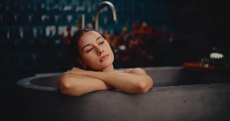 A serene young woman peacefully relaxes in a modern, luxurious concrete bathtub