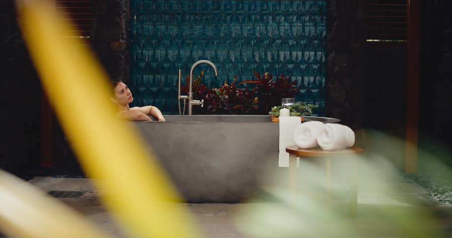 A woman peacefully relaxes in a stylish outdoor bathtub at a luxury spa