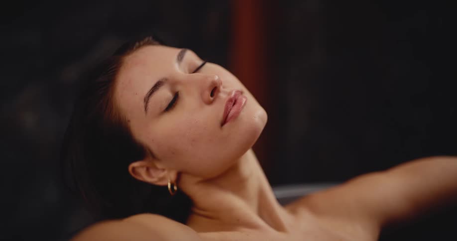 A close-up of a serene woman with wet hair closing her eyes in a tranquil, steamy spa