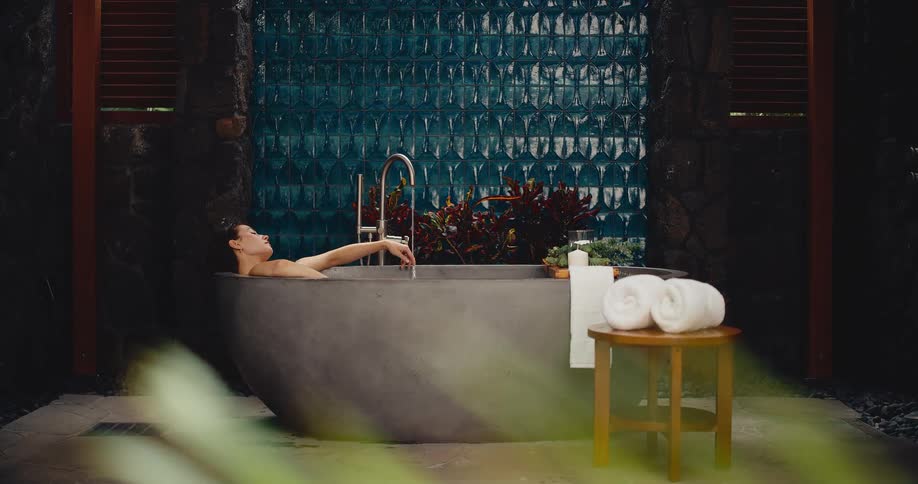 Woman finds tranquility while relaxing in a luxurious stone bathtub in a serene outdoor spa setting