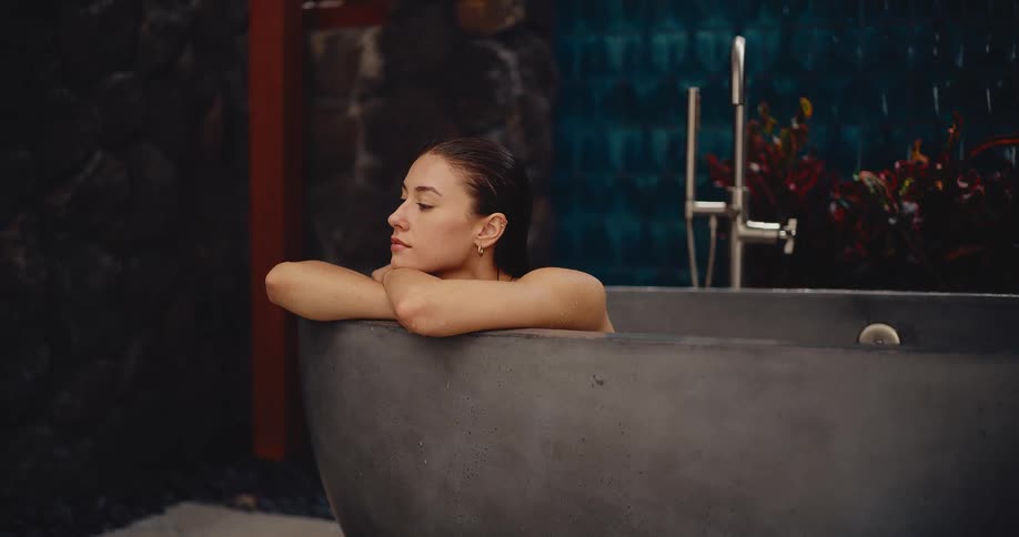 A beautiful young woman relaxes and unwinds in a modern stone bathtub at a luxury spa