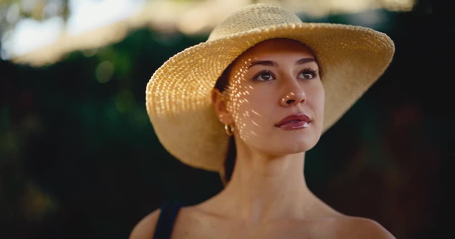Cinemagraph of a fashionable woman in a straw sun hat with dappled sunlight patterns on her face