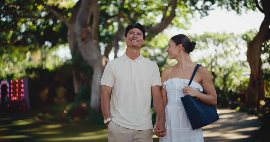 A romantic young couple holds hands and smiles while walking through a beautiful park in slow motion