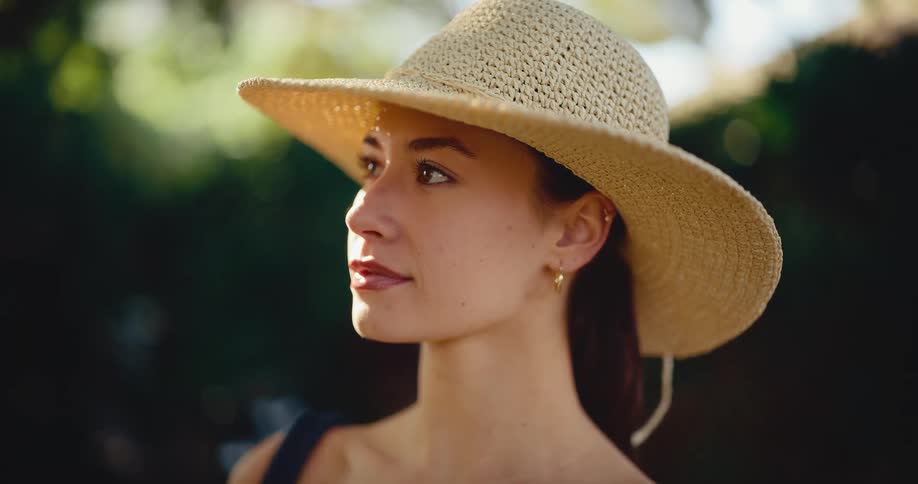 An elegant young woman in a straw hat gazes serenely into the distance, her face illuminated by the warm golden hour light