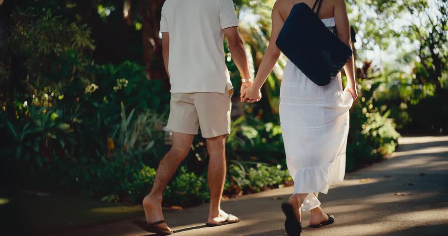 A romantic couple holds hands while walking together down a beautiful path in a tropical resort
