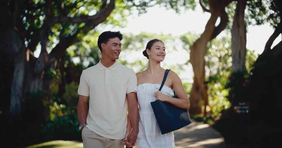 A romantic couple enjoys a slow-motion walk together, holding hands down a beautiful tree-lined path