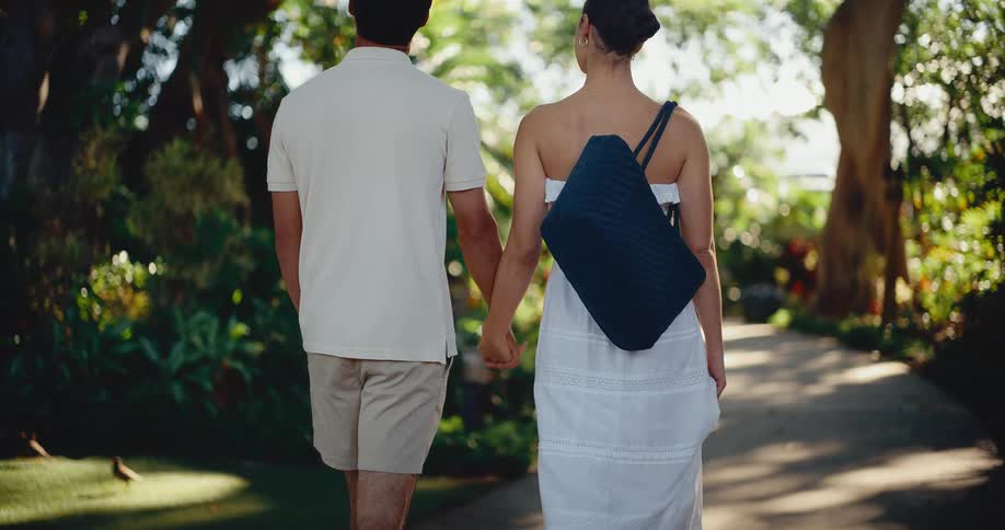 A man and woman hold hands and walk down a lush green path at a tropical resort in slow motion