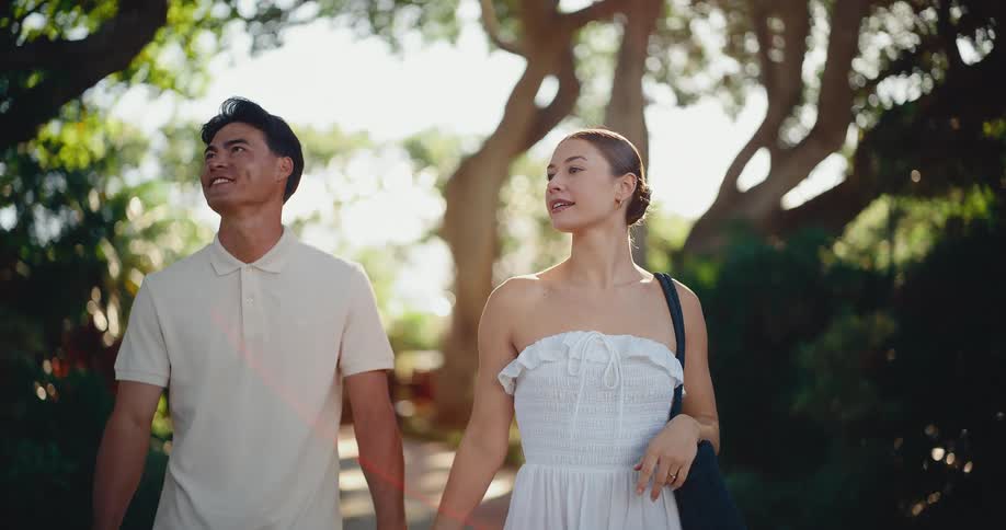 Cinematic slow motion of a beautiful couple holding hands and strolling down a sun-drenched, tree-lined path