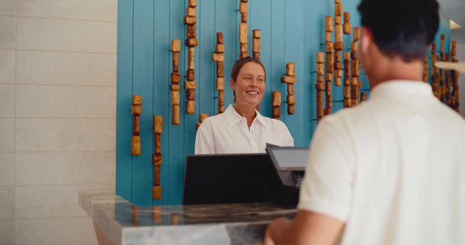 A friendly hotel receptionist smiles and chats with a male guest at the front desk of a modern resort