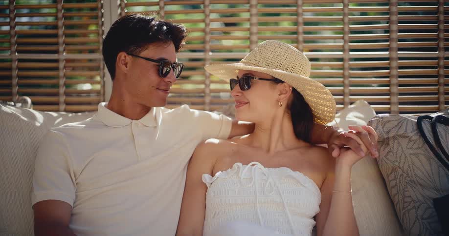 An elegant couple in sunglasses and summer attire relaxes together, sharing a romantic moment in the sun