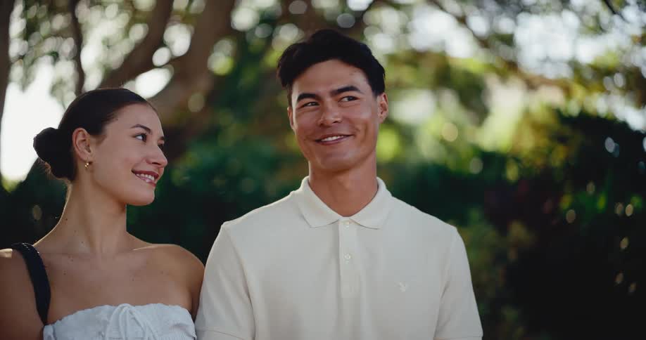 A romantic couple looks lovingly into each other's eyes while standing in a lush green park during golden hour
