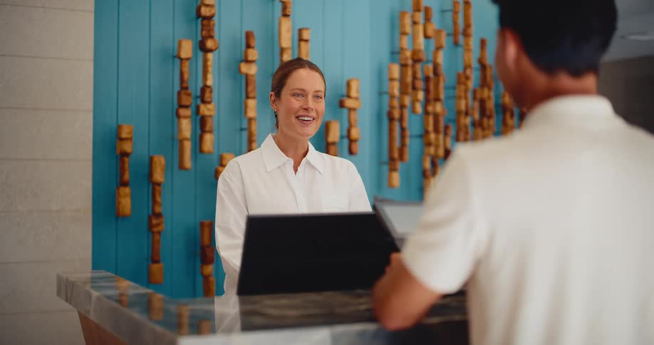 A friendly hotel receptionist smiles and chats with a guest at the check-in counter