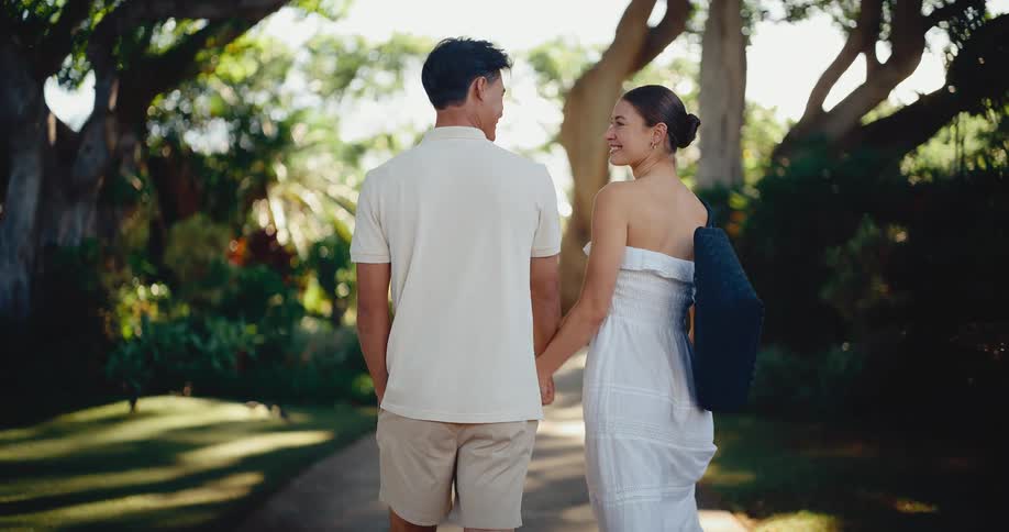 A happy couple holds hands while taking a romantic stroll down a beautiful tree-lined path at a tropical resort