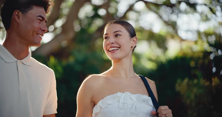 A beautiful young woman smiles lovingly at her partner while they enjoy a romantic walk through a sunlit park