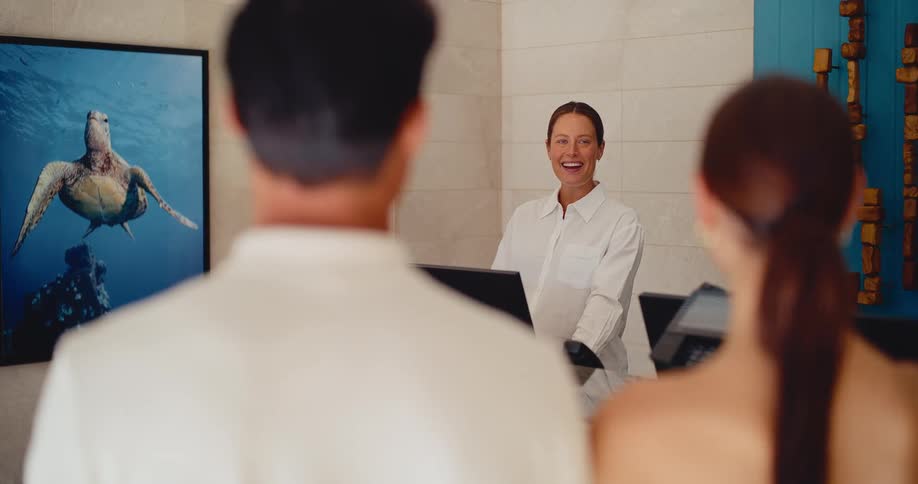 A friendly hotel receptionist smiles warmly while checking in a couple at the front desk