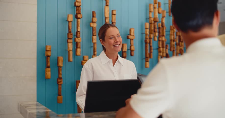 A friendly female hotel receptionist smiles as she assists a male guest at the check-in counter in a stylish lobby