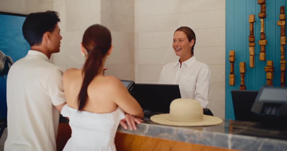 A friendly hotel receptionist welcomes a young couple as they check in for their vacation