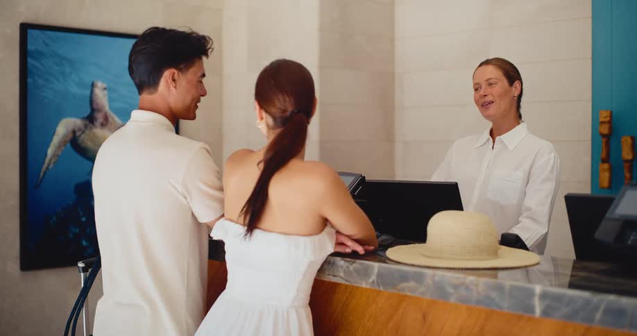 A happy couple on vacation checks into a luxury hotel and talks with the friendly receptionist at the front desk