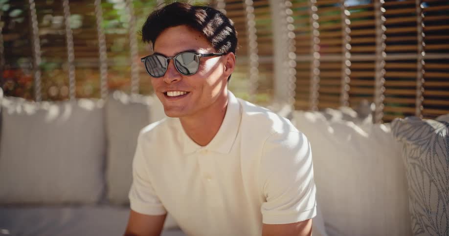 Portrait of a happy young man in a white polo shirt and sunglasses relaxing on a luxurious outdoor sofa on a sunny day