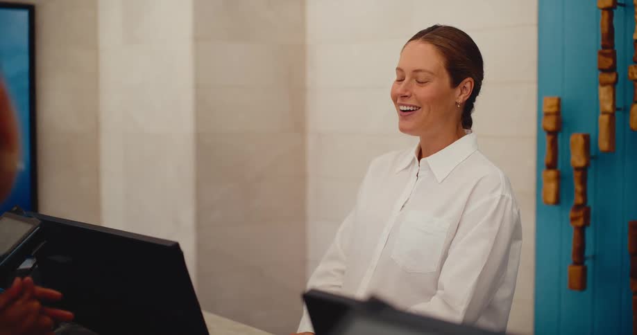 A friendly hotel receptionist with a bright smile cheerfully assists a guest at the front desk