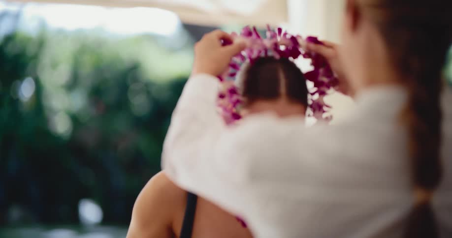 A smiling young woman is welcomed to a tropical destination as another woman places a traditional Hawaiian flower lei around her neck in slow motion