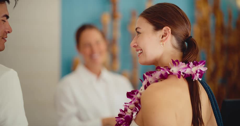 A friendly hotel concierge welcomes a smiling female guest by placing a beautiful flower lei around her neck in slow motion