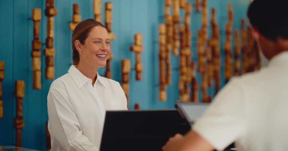 A friendly female concierge smiles and laughs while assisting a male guest at the hotel check-in desk