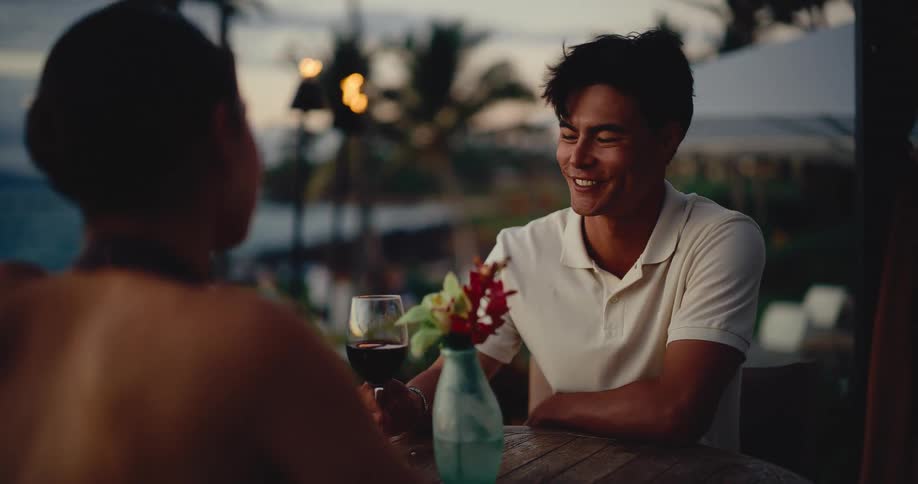 Over-the-shoulder view of a handsome man smiling at his date during a romantic dinner at a tropical resort
