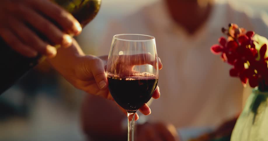 A close-up slow-motion shot of red wine being poured into a wine glass during a romantic sunset dinner