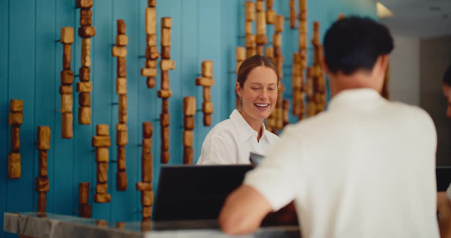 A smiling and friendly hotel receptionist helps a guest at the front desk of a stylish luxury hotel