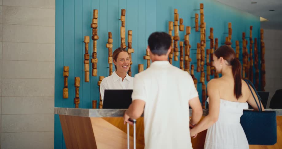 A friendly hotel receptionist welcomes an arriving couple as they check into a stylish luxury resort for their vacation