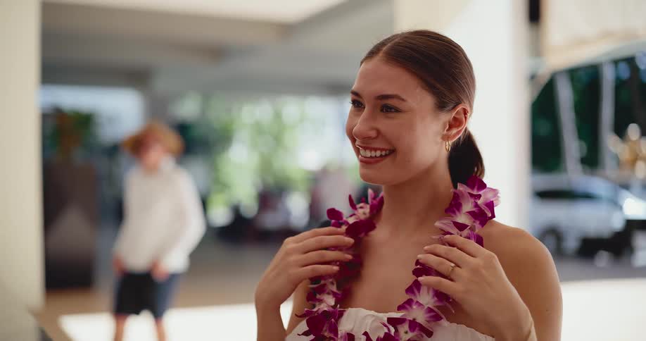 A man welcomes a smiling woman to a tropical resort by placing a beautiful purple orchid lei around her neck in slow motion
