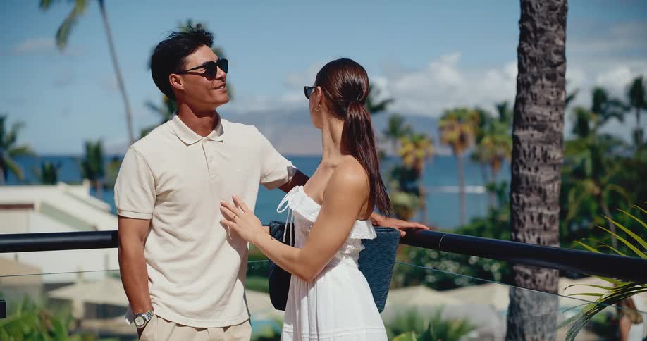 A stylish young couple in love enjoys a romantic moment on a sunny balcony overlooking the ocean at a luxury tropical resort