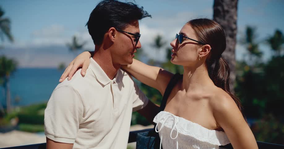An attractive young couple embraces and looks at each other lovingly on a sunny balcony at a tropical resort