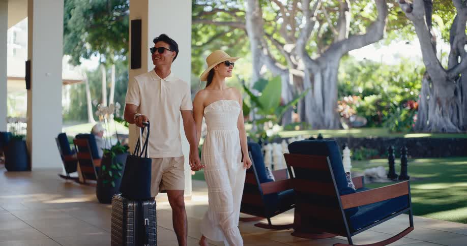 Happy attractive couple walking through a hotel lobby, arriving for their tropical vacation