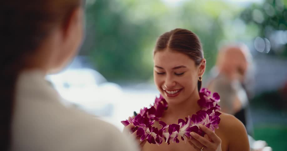 A young woman is warmly welcomed with a traditional Hawaiian purple orchid lei placed around her neck in slow motion