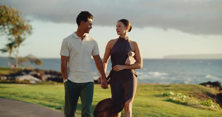 Attractive couple walking hand in hand together by the ocean at sunset in slow motion