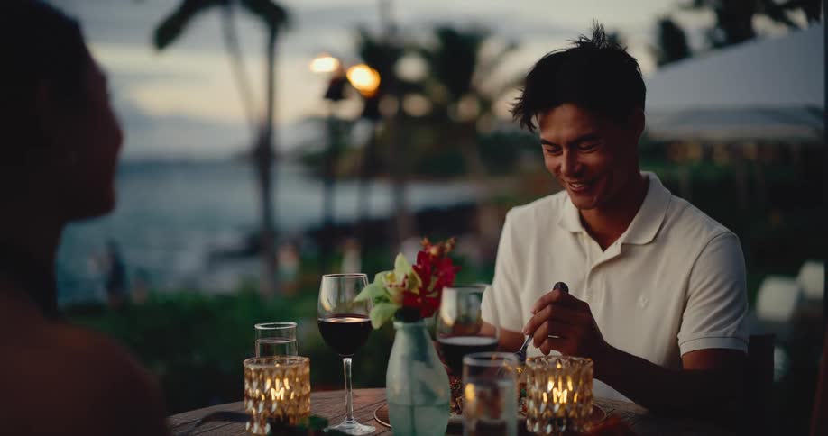 Handsome young man smiling and enjoying a romantic dinner with his date at a beautiful beachside restaurant at sunset