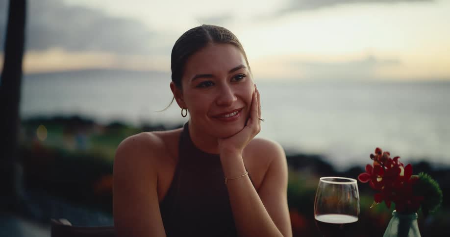 A beautiful young woman smiles happily during a romantic sunset dinner with a view of the ocean