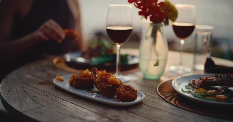 A beautifully plated appetizer is served at an elegant outdoor dinner for two with red wine at sunset