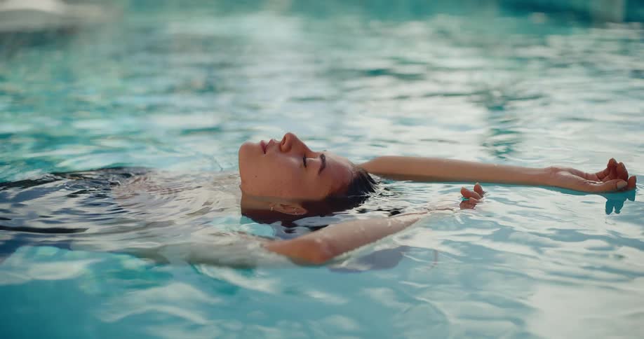 A serene woman floats peacefully on her back in the calm water of a swimming pool, enjoying a moment of relaxation