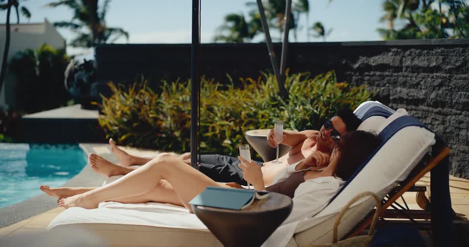 Happy couple relaxing on vacation, lounging by the pool and toasting with champagne